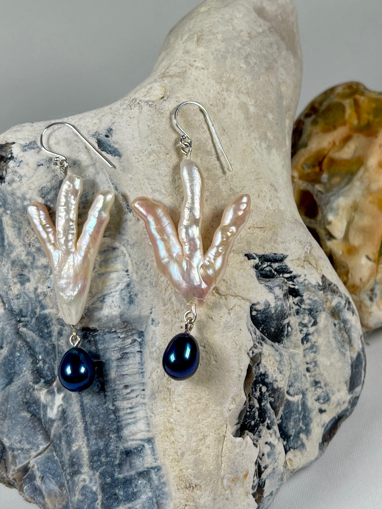 Silver dangly Earrings with a white pearl in the shape of a claw with a dark blue coloured  pearl