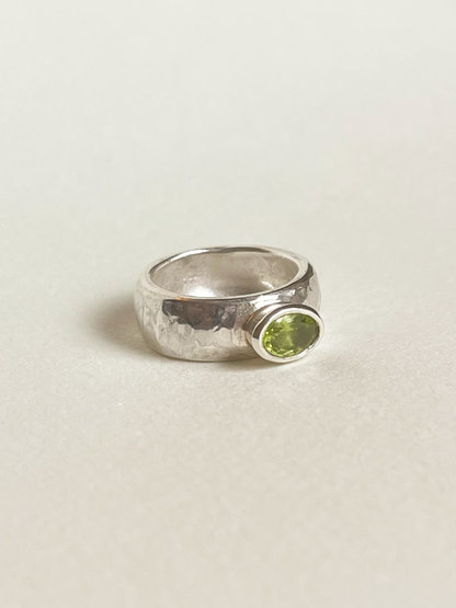 Chunky silver ring with a green peridot on a light background