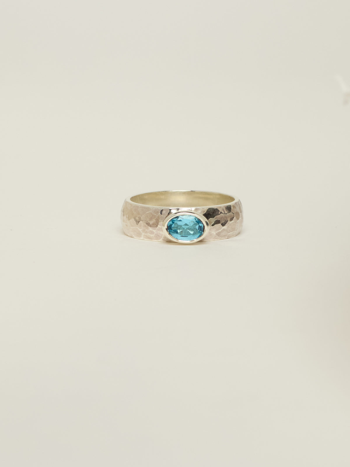 A hammered silver ring featuring an oval swiss topaz gemstone in a bezel setting, centred against a plain off-white background.