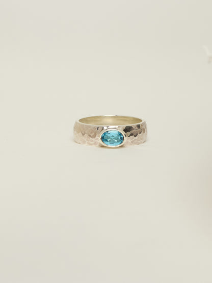 A hammered silver ring featuring an oval swiss topaz gemstone in a bezel setting, centred against a plain off-white background.