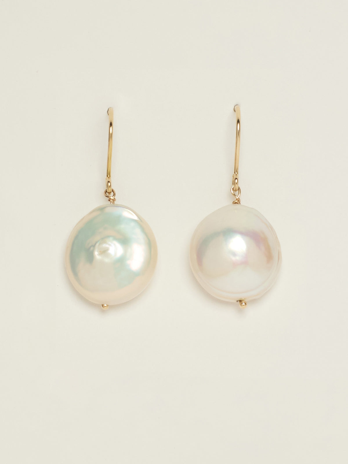 A pair of gold drop earrings featuring large, lustrous baroque pearls with iridescent white, pink, and green hues, displayed on a clean off-white background.