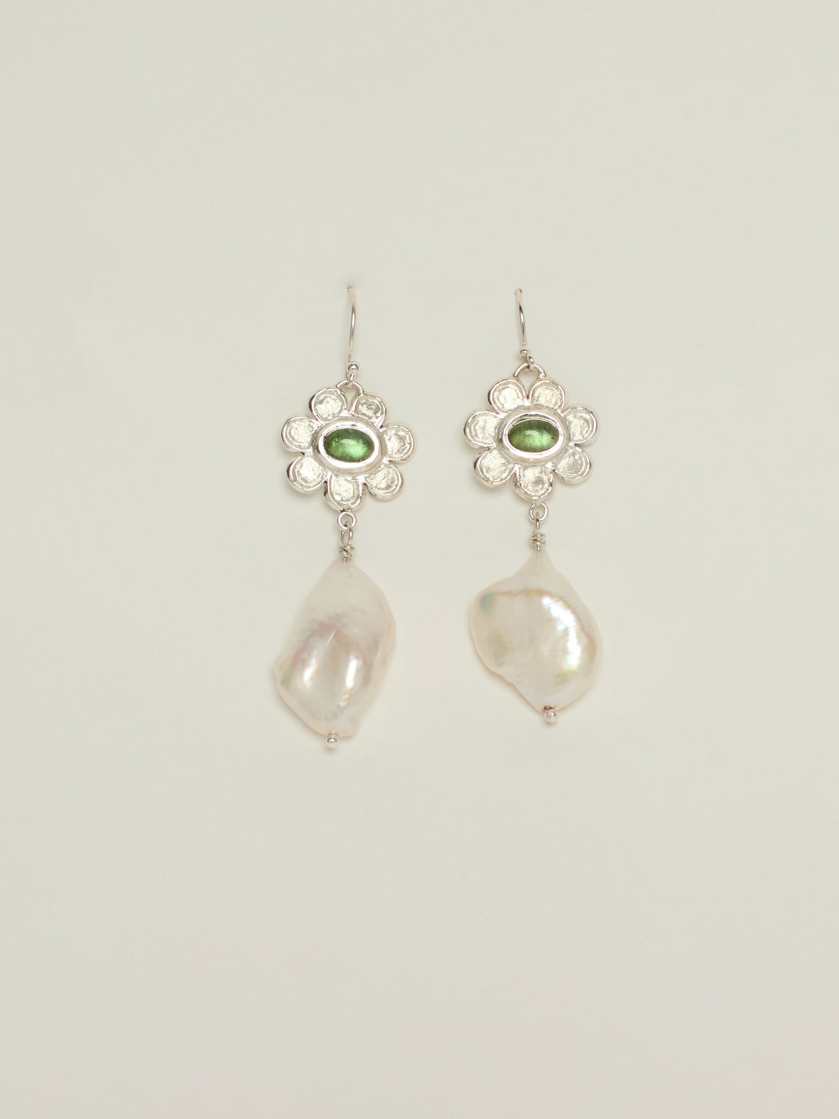 A pair of silver dangle earrings featuring a small oval green tourmaline stone in a floral setting, with a large, irregular white baroque pearl hanging below, shown against a light gray background.