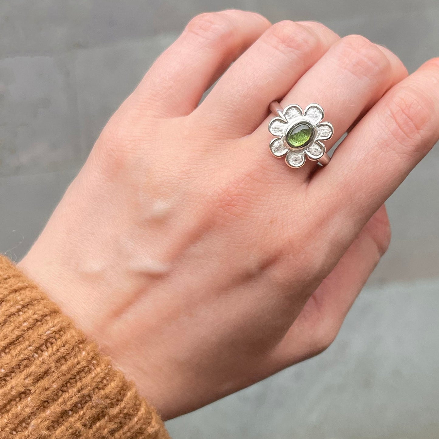 Hand wearing a silver ring with a green tourmaline against a neutral background
