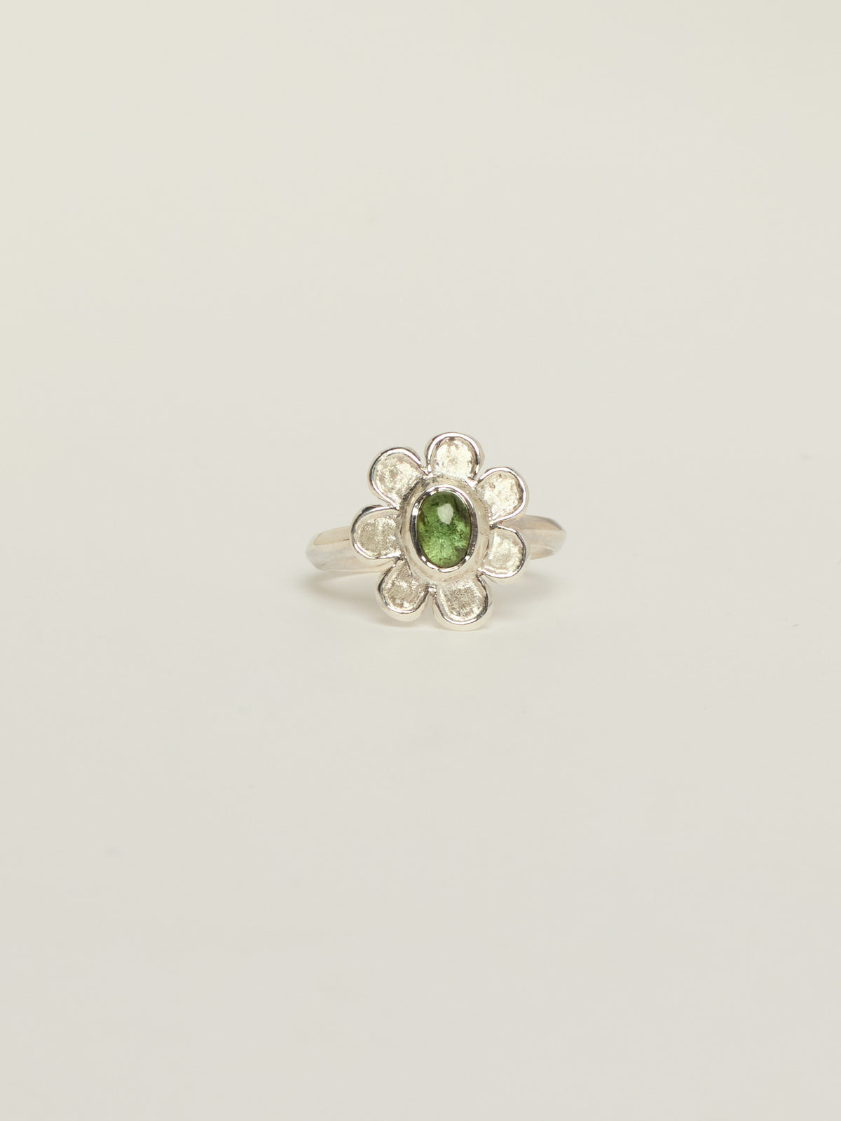 A silver flower ring featuring a central green oval tourmaline, set against a plain light gray background.