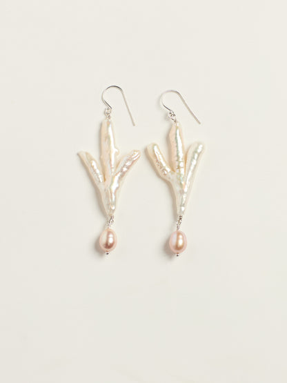 A pair of dangle earrings featuring natural baroque pearls arranged in a claw like shape, with a small teardrop pearl hanging below each, suspended from silver fishhook wires on a light beige background.