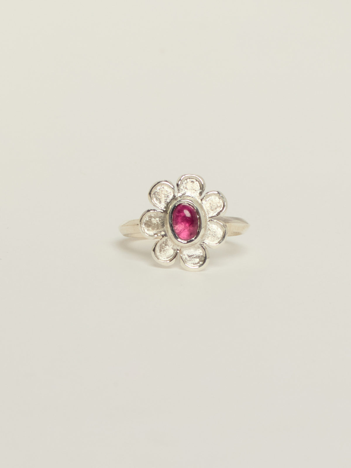 A silver flower ring featuring a central oval pink tourmaline, set against a plain light gray background.