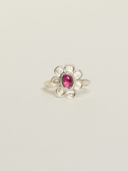 A silver flower ring featuring a central oval pink tourmaline, set against a plain light gray background.