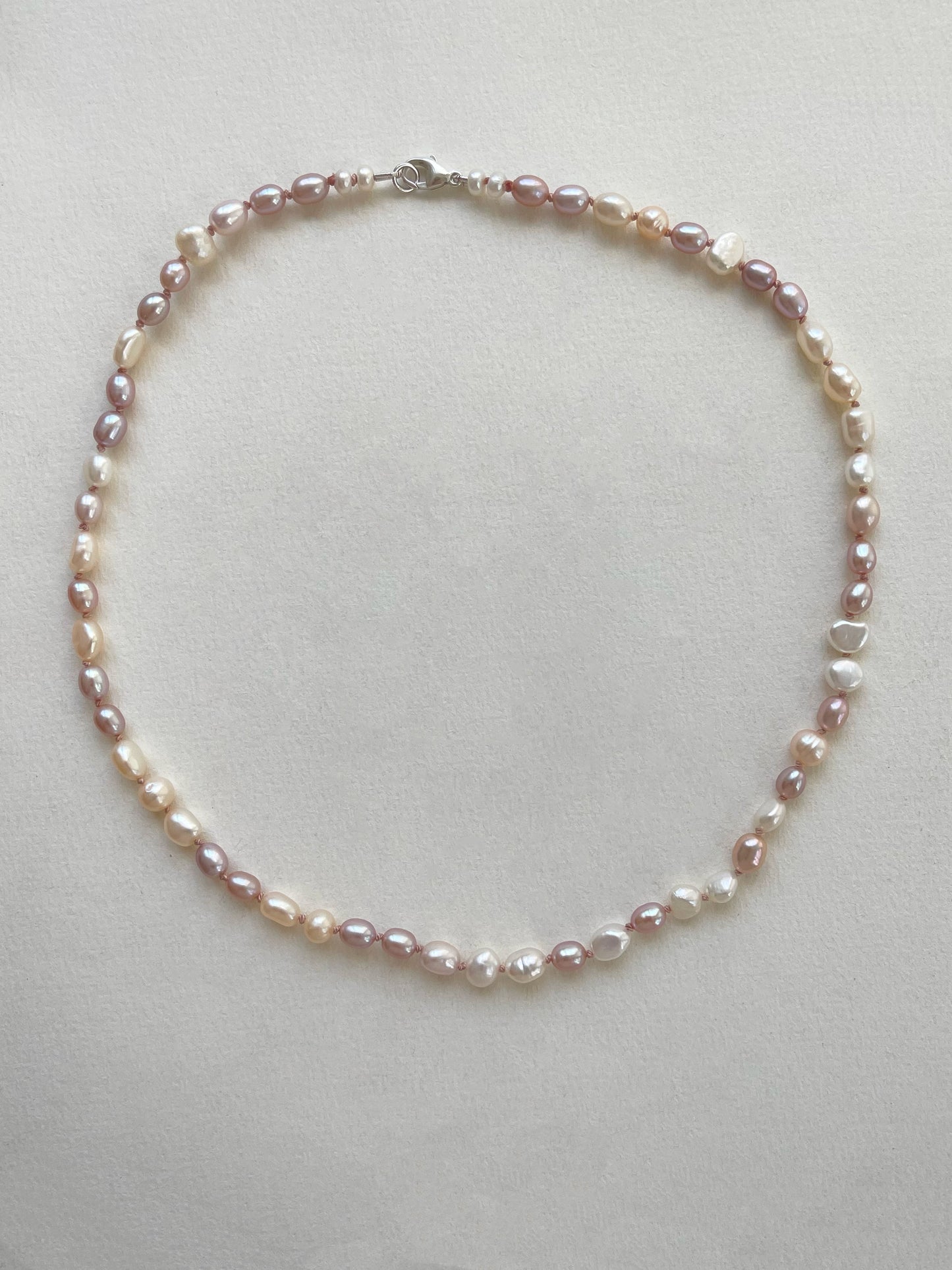 Pearl necklace of white and pink pearls on a light grey background