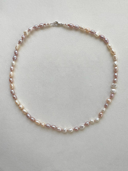 Pearl necklace of white and pink pearls on a light grey background