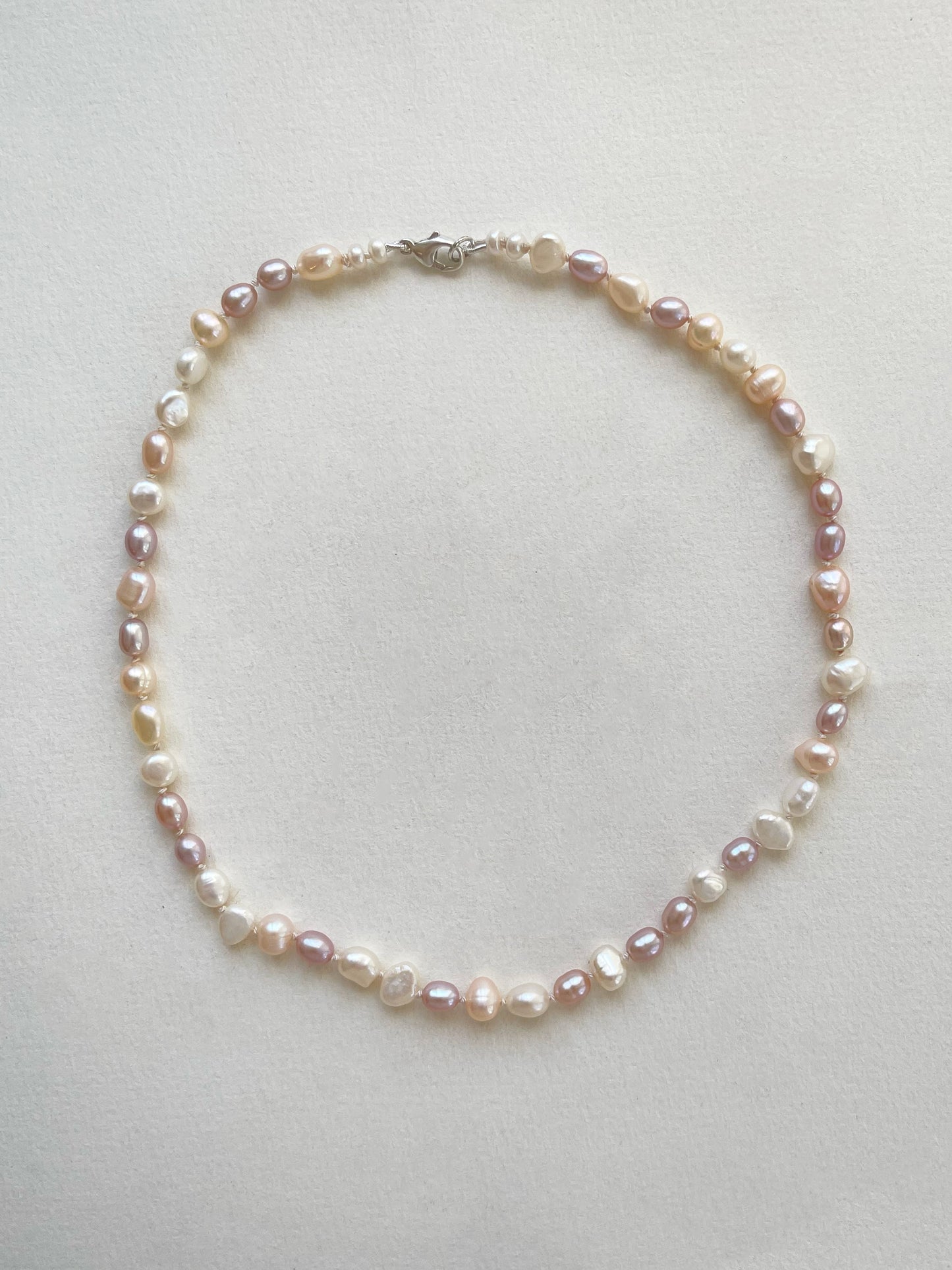 Pearl necklace of white and pink pearls on a light gray background