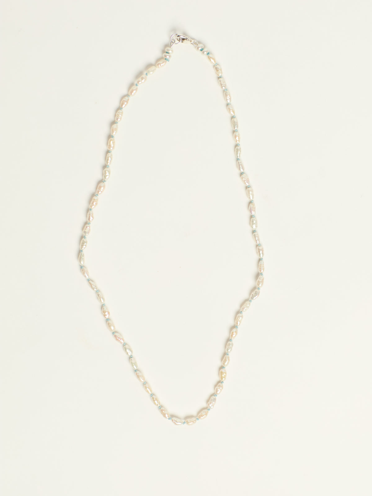 A delicate necklace with small, irregular white pearls, arranged in a vertical loop on a clean, off-white background.