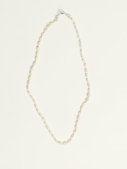 A delicate necklace with small, irregular white pearls, arranged in a vertical loop on a clean, off-white background.