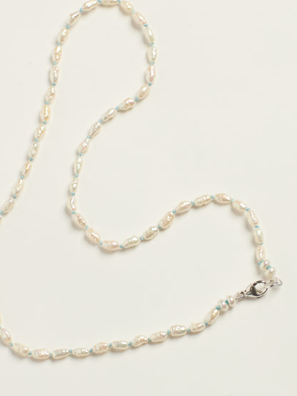 A delicate beaded necklace featuring irregular, pearly off-white baroque pearls separated by thin light blue threads, finished with a silver lobster clasp, laid out on a clean white background.