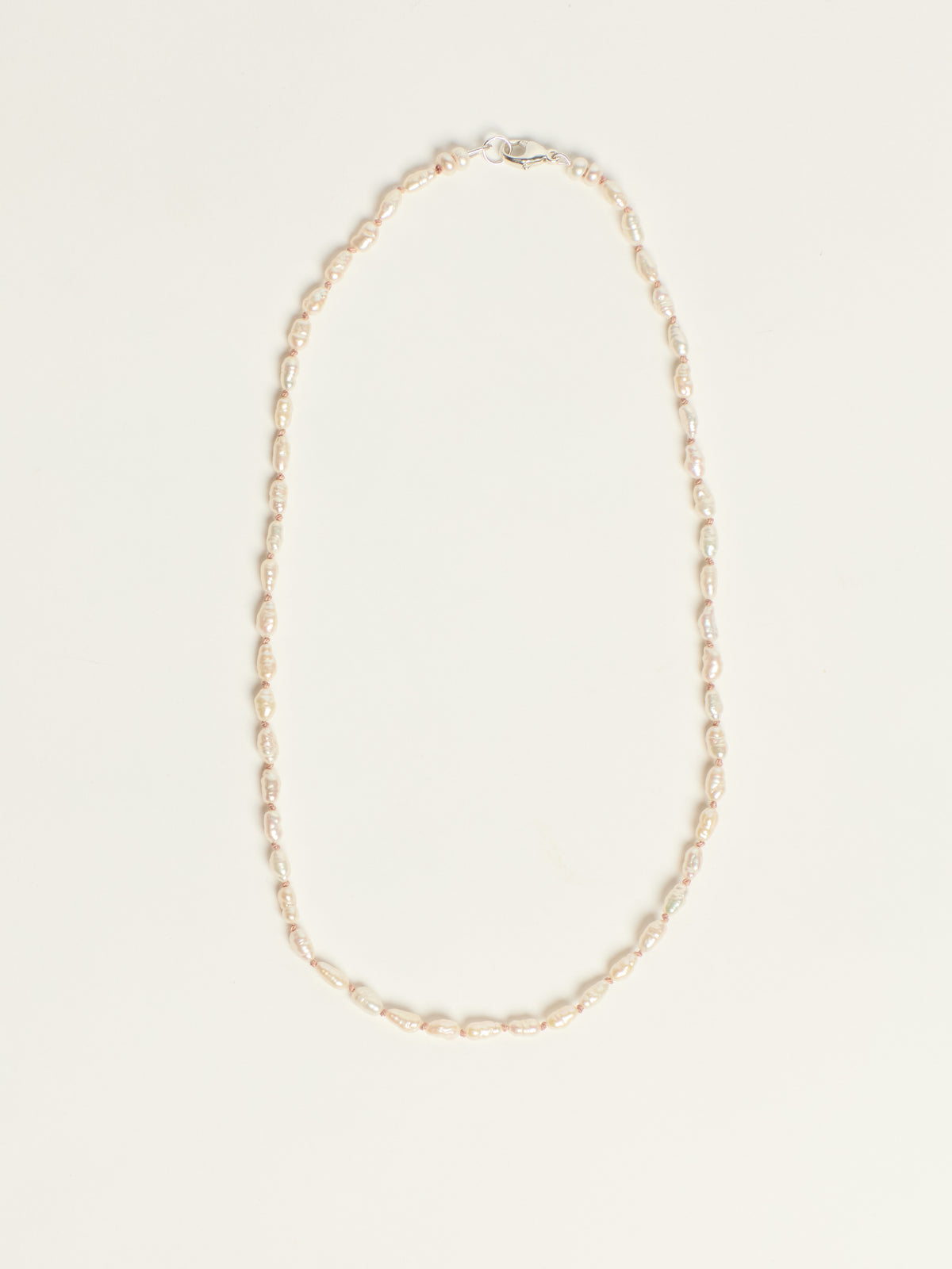 A delicate gold chain necklace with a lobster clasp, laid flat on a light cream background.