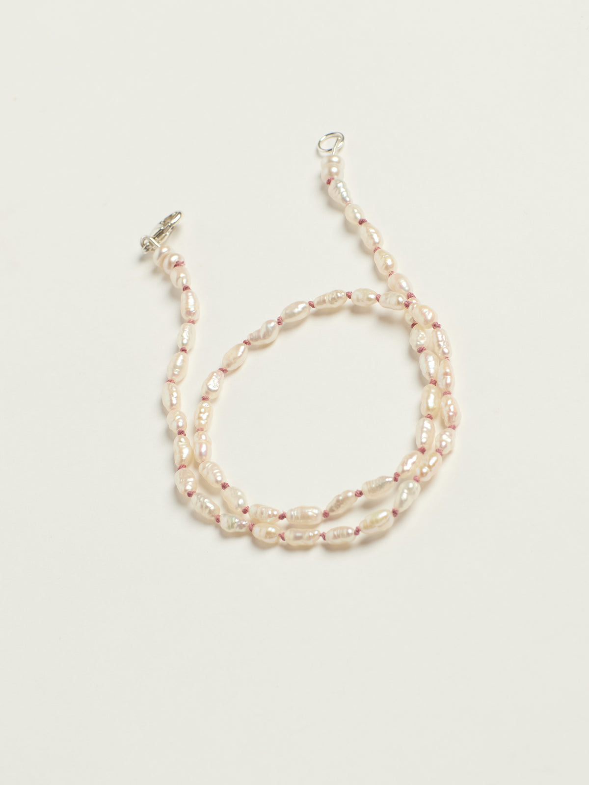 A double-strand beaded necklace featuring irregular cream-colored baroque pearls separated by small pink beads, finished with a silver clasp, shown on a light cream background.