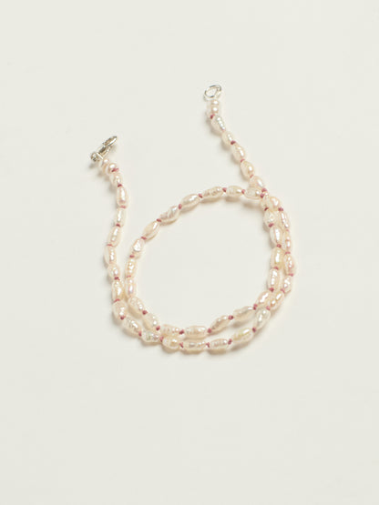 A double-strand beaded necklace featuring irregular cream-colored baroque pearls separated by small pink beads, finished with a silver clasp, shown on a light cream background.
