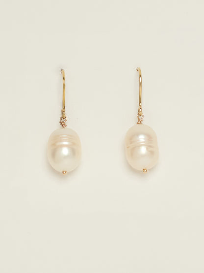 A pair of gold drop earrings featuring large, lustrous pearls with iridescent white and pink hues, displayed on a clean off-white background.