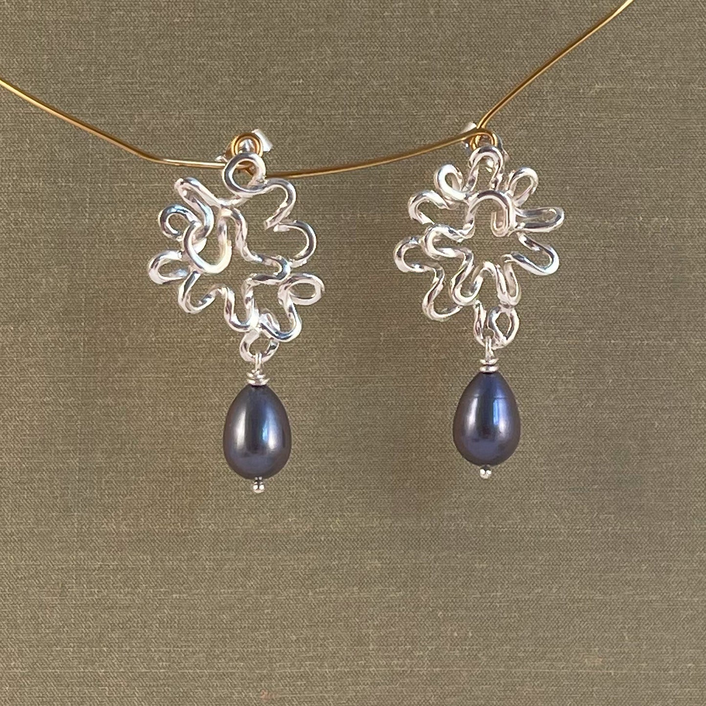 Silver earrings with blue Pearl on a gold chain against a green background