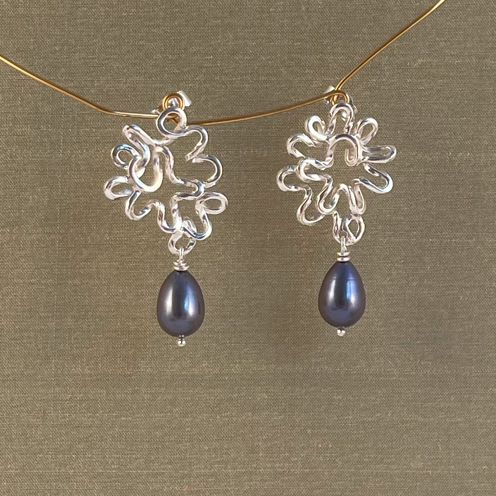 Silver earrings with blue Pearl on a gold chain against a green background