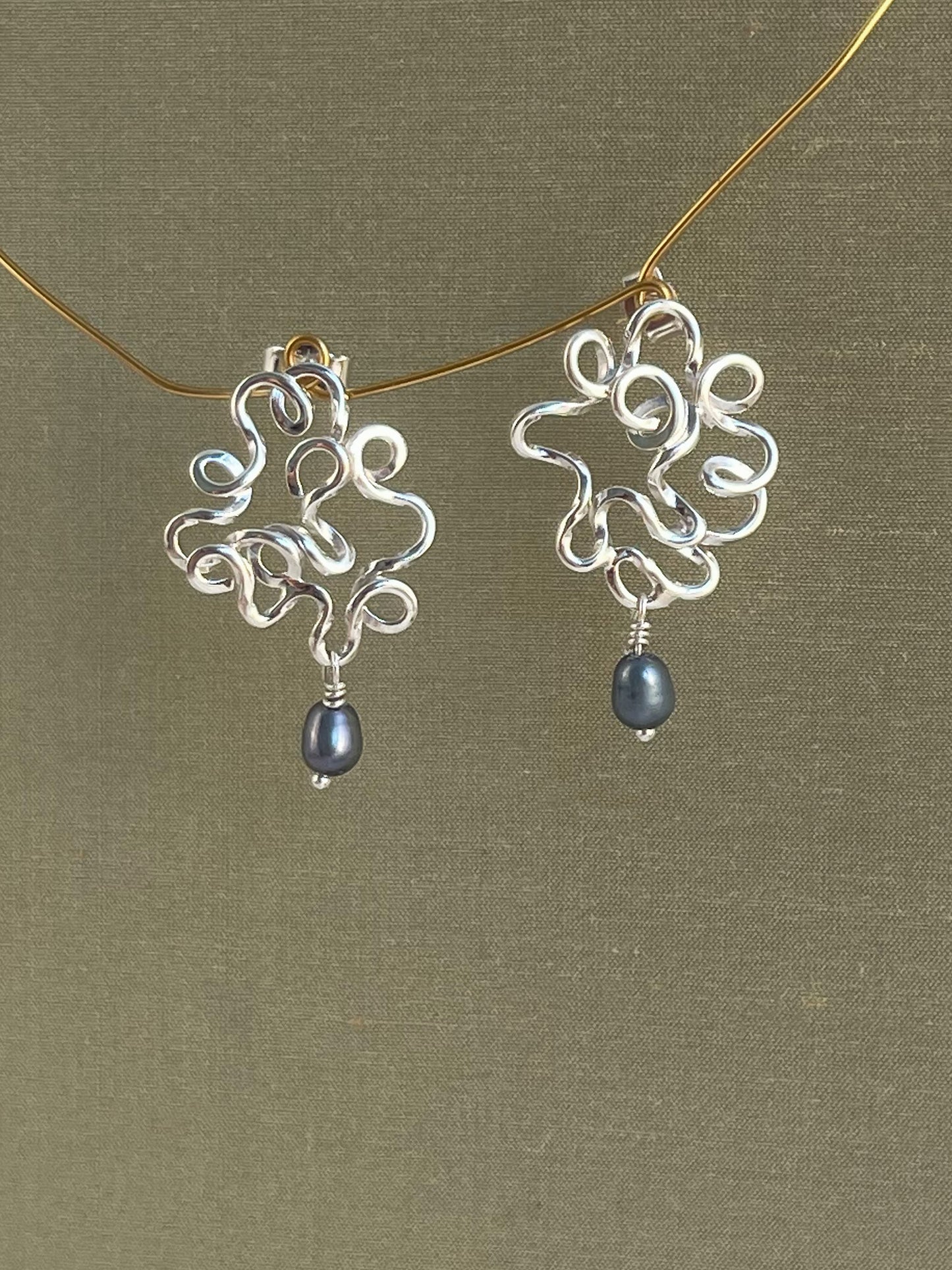 Silver earrings with blue pearls on a gold chain against a green background