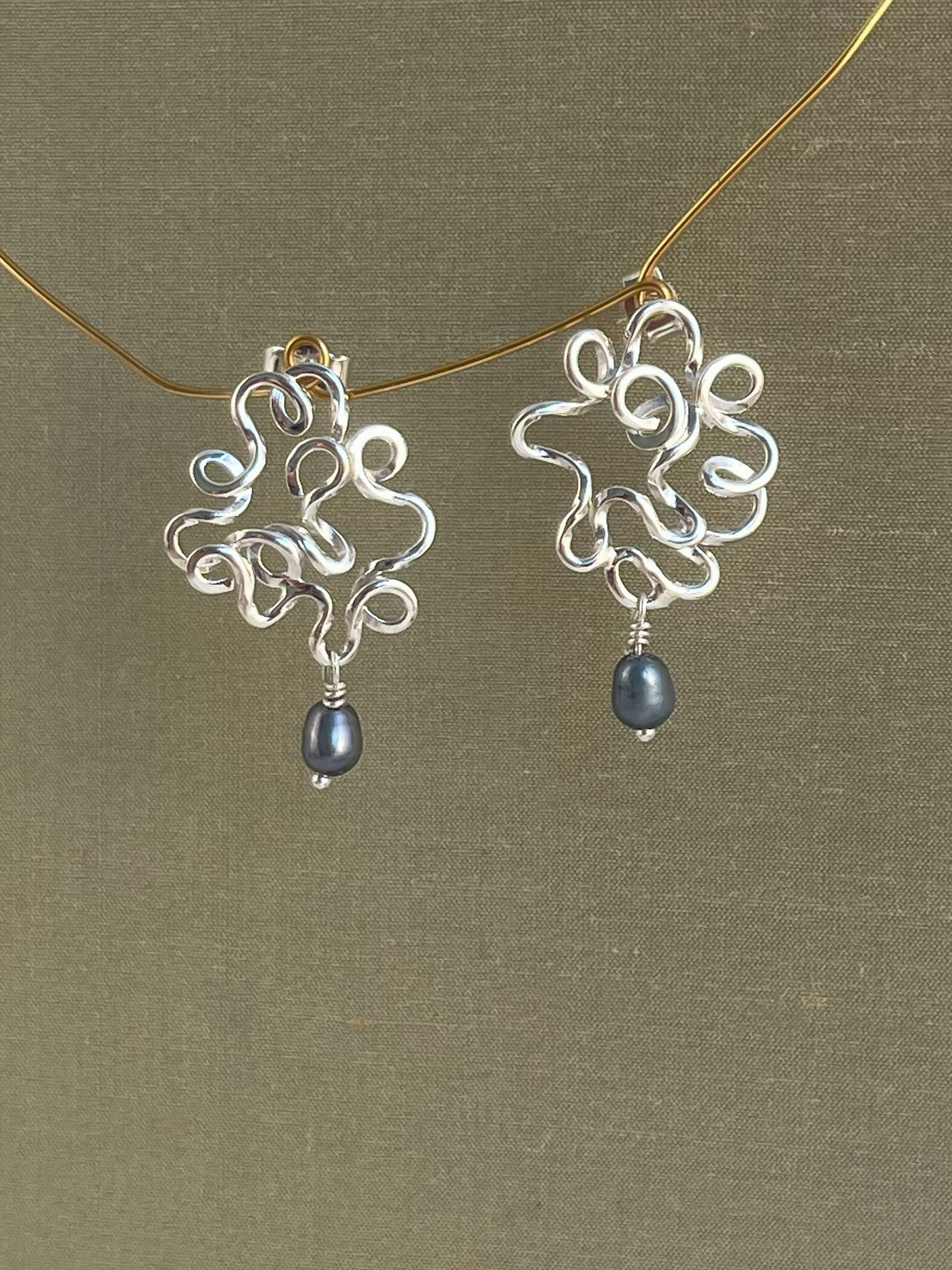 Silver earrings with blue pearls on a gold chain against a green background