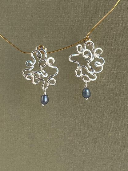Silver earrings with blue pearls on a gold chain against a green background
