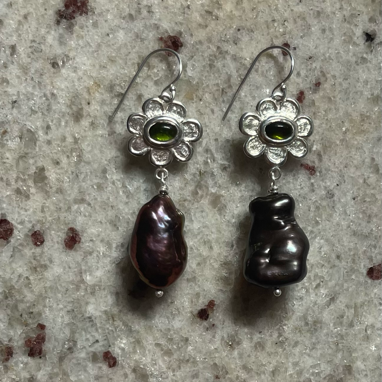 Pair of silver earrings with Black baroque pearls set with green tourmaline stones on a textured surface